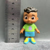 A playful cartoon PVC figurine of a boy with dark skin, wearing a green shirt and blue shorts, standing next to a ruler.