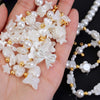 A hand holds a collection of white and cream pearl beads, including star and bow shapes, with gold accents.