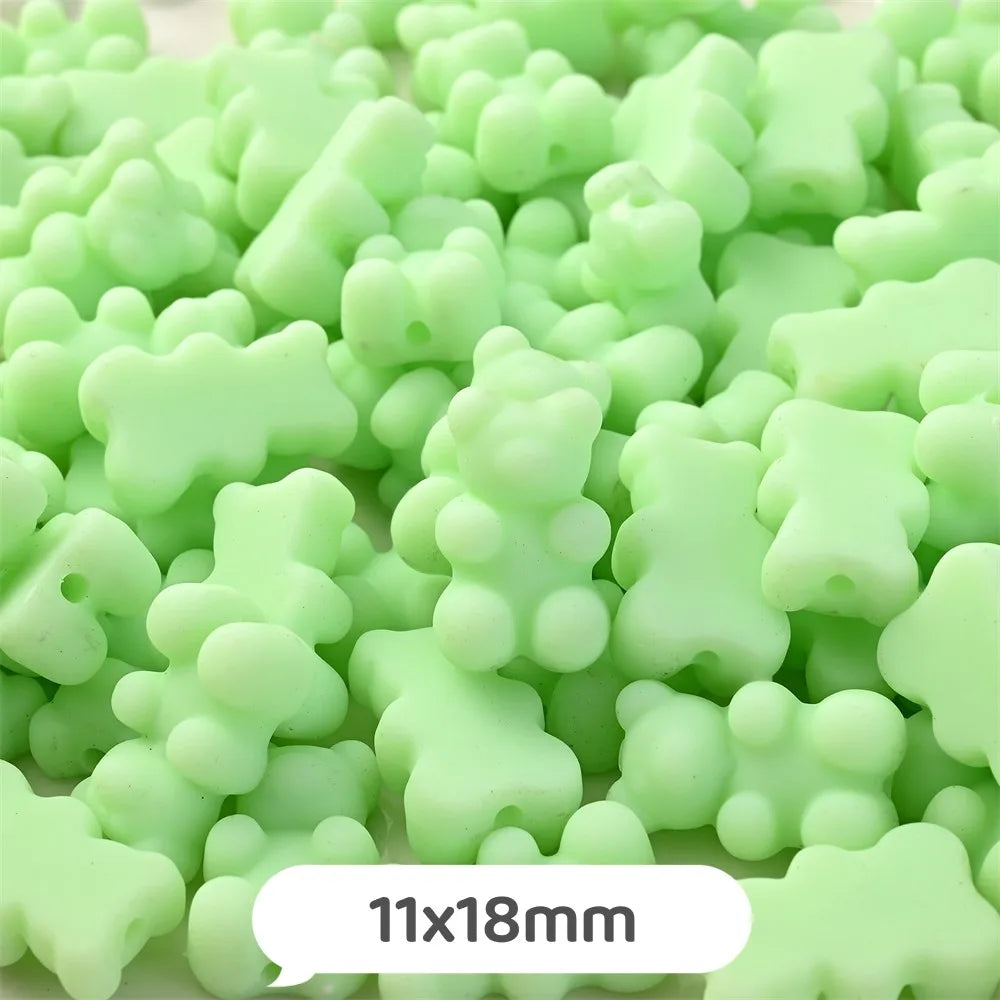 A pile of pastel green bear-shaped acrylic craft beads with a shimmer finish.