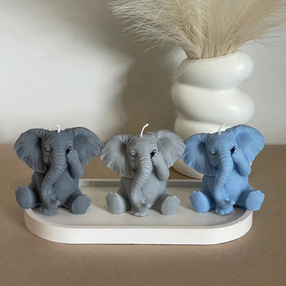 Three silicone elephant molds in gray and blue sitting on a white tray with a white vase in the background
