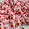 A pile of handmade crochet mini pig keychains in various shades of pink and red.