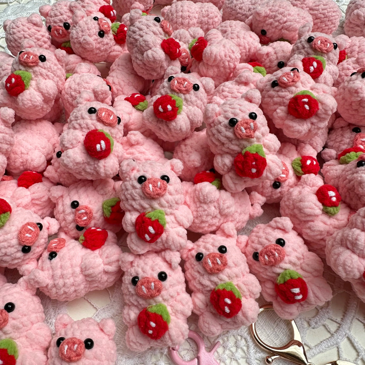 A pile of handmade crochet mini pig keychains in various shades of pink and red.