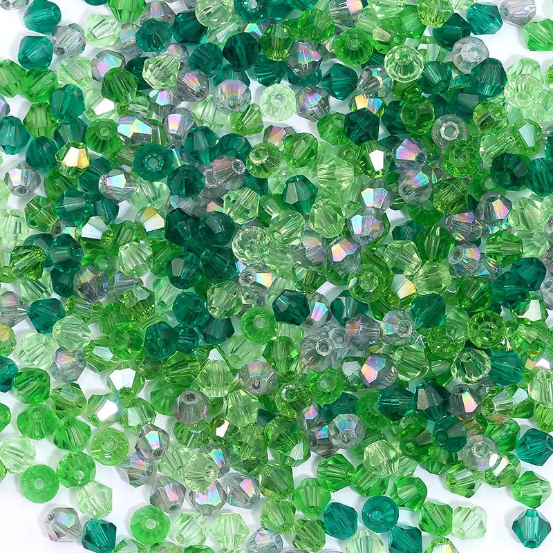 A pile of faceted green and purple bicone glass beads for jewelry making.