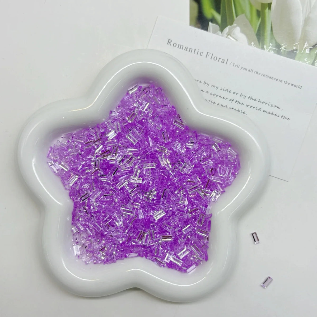 A white flower-shaped container filled with purple glitter ice strips for nail art and DIY crafts.