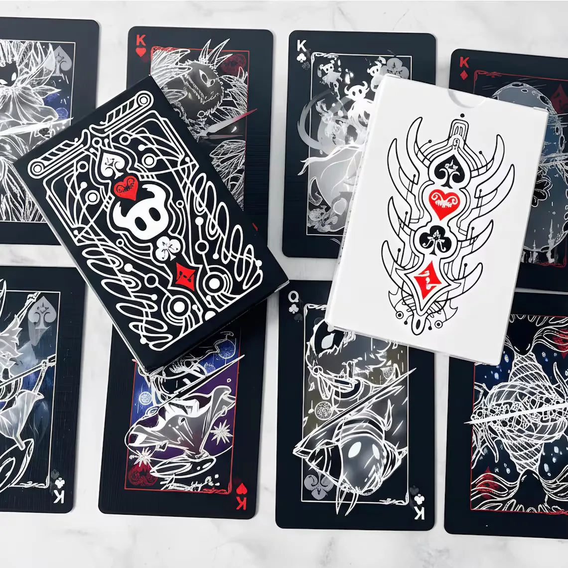 A collection of black and white poker card decks featuring Hollow Knight artwork displayed on a white marble surface.