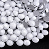 A close-up view of various flatback rhinestones in silver and white shades scattered on a dark surface.
