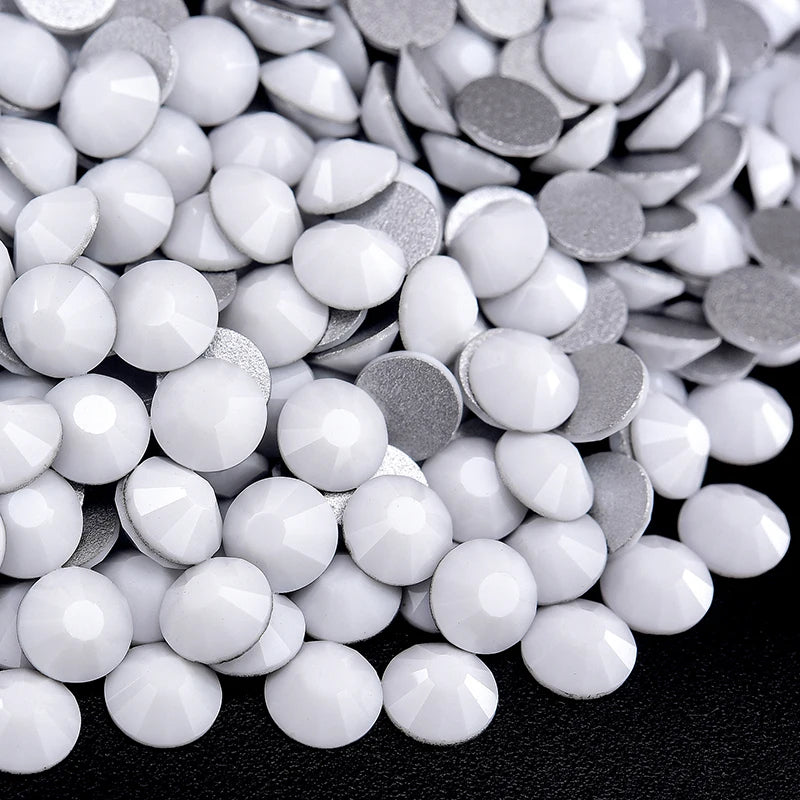 A close-up view of various flatback rhinestones in silver and white shades scattered on a dark surface.