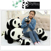 A woman is sitting on a bed with two panda plush toys, one of which is being held to her chest.