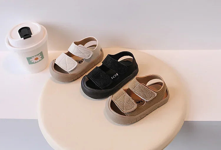 A set of toddler soft-soled sandals for boys and girls in beige and black colors displayed on a white surface.
