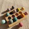 A wooden stacking block set featuring various pastel colored spheres arranged in a tray on a light fabric surface.