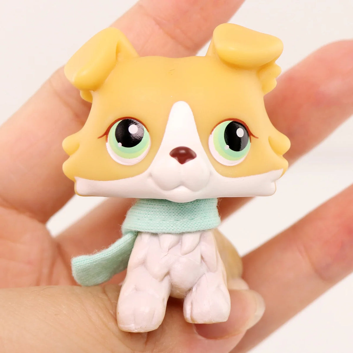 A miniature pet animal figure of a yellow dog with white markings and light green accessories being held in a hand.
