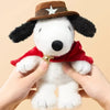 A white plush doll resembling a dog wearing a brown cowboy hat and a red bandana, held by two hands.