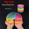 A hand is holding a colorful, elastic rainbow circle toy with bright stripes.