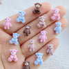 A collection of small resin teddy bear charms in various shades of pink and blue displayed on a hand.