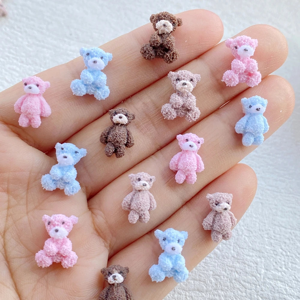 A collection of small resin teddy bear charms in various shades of pink and blue displayed on a hand.