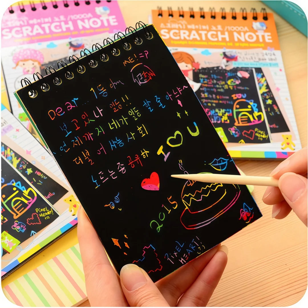 A hand holds a black scratch note book with colorful drawings and text, next to other scratch notes.
