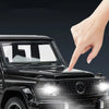 A hand points to the front of a black diecast RV camper truck model with illuminated headlights.