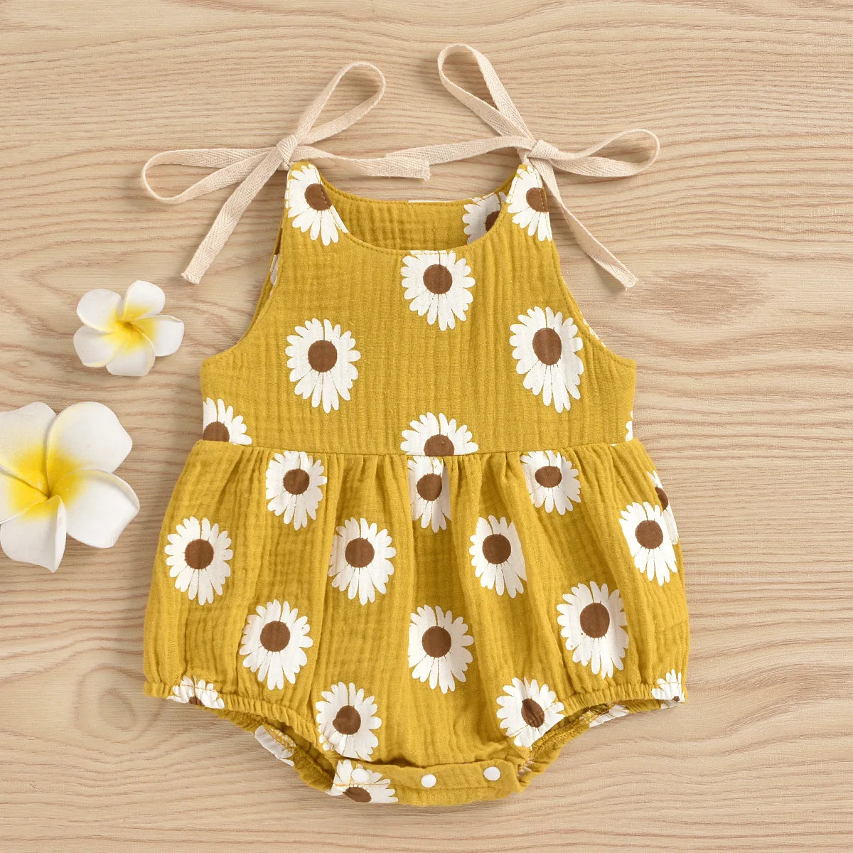 A yellow cotton romper for a baby girl with a white daisy floral print and adjustable ties.