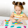 A young girl is assembling a wooden geometric shape puzzle on a white table.