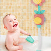 A baby is playing with a pink and yellow sunflower bath shower sprinkler toy in a bathtub.