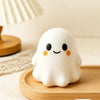A white, squishy ghost-shaped stress ball rests on a wooden tray next to a lamp.