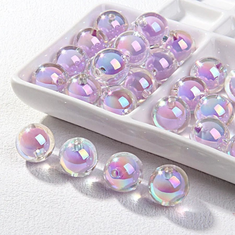 A white tray filled with various iridescent purple and pink acrylic craft beads for jewelry making.