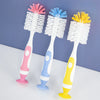 A set of three silicone baby bottle cleaning brushes in pink, blue, and yellow with suction stands.