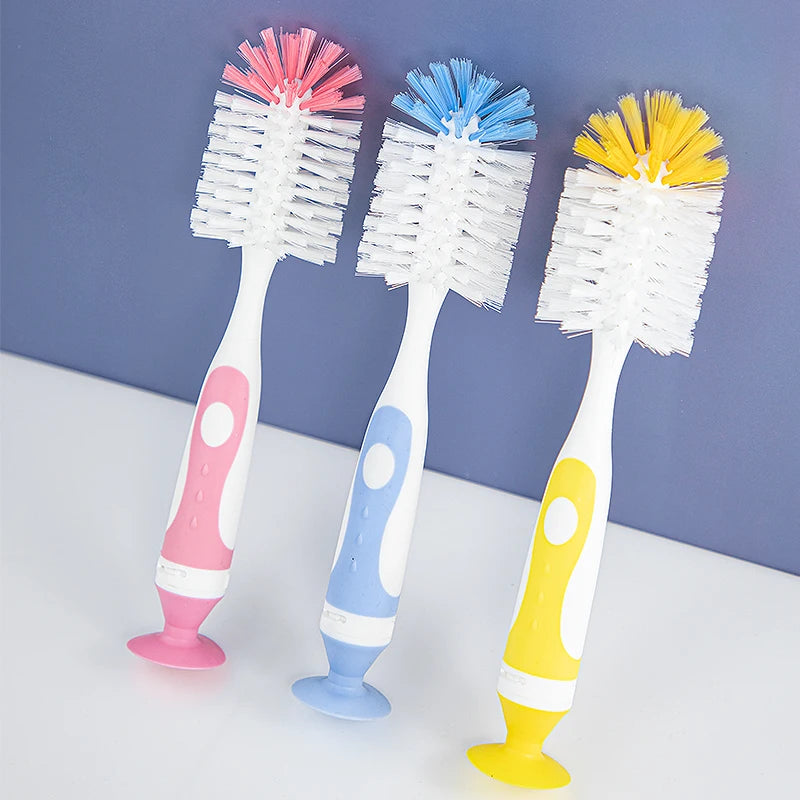 A set of three silicone baby bottle cleaning brushes in pink, blue, and yellow with suction stands.