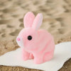 A pink electric plush rabbit toy with long ears sitting on a white surface against a sandy background.