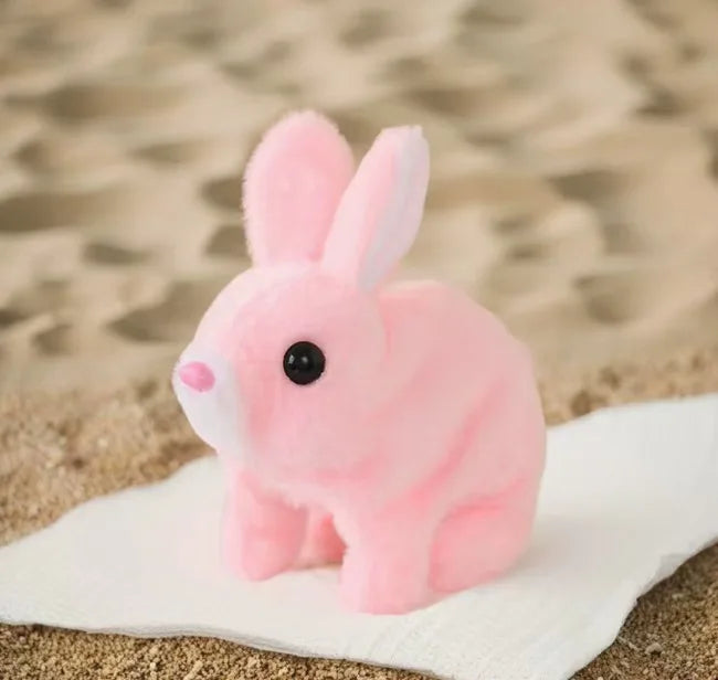 A pink electric plush rabbit toy with long ears sitting on a white surface against a sandy background.