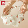A pair of white cotton gauze baby bandana bibs with pink strawberry patterns being held by a hand under water.