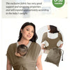 A woman is wearing a beige X-shaped baby sling carrier while holding a baby.