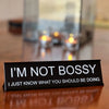 Black desk sign with white text that reads I'M NOT BOSSY and I JUST KNOW WHAT YOU SHOULD BE DOING