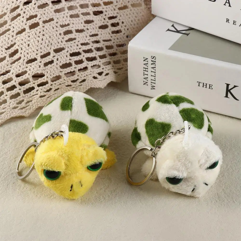 A pair of adorable green and white turtle plush keyrings with gold-colored metal rings resting on a light surface.