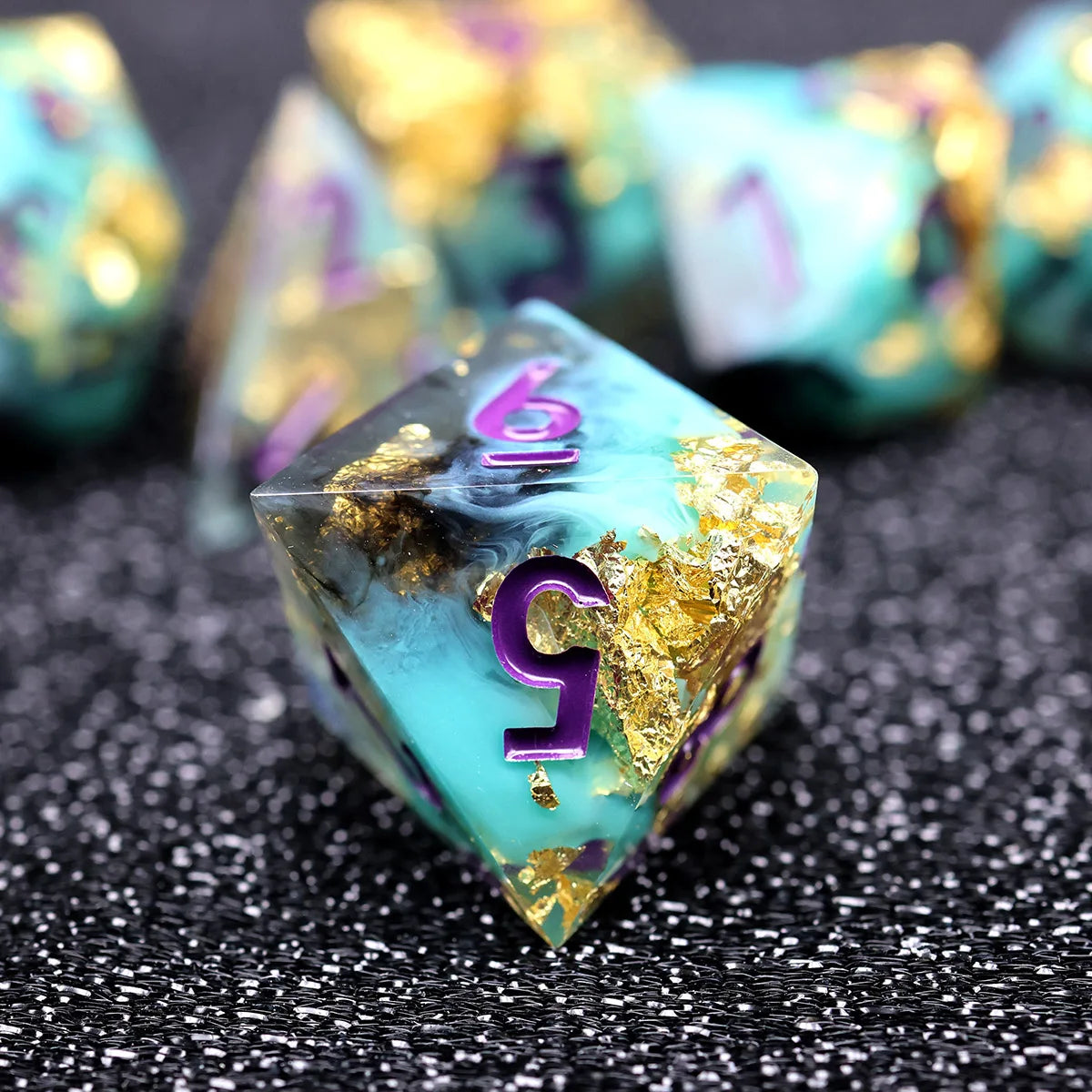 A close-up of a translucent teal polyhedral die showing the number 5, set against a dark background with other dice.
