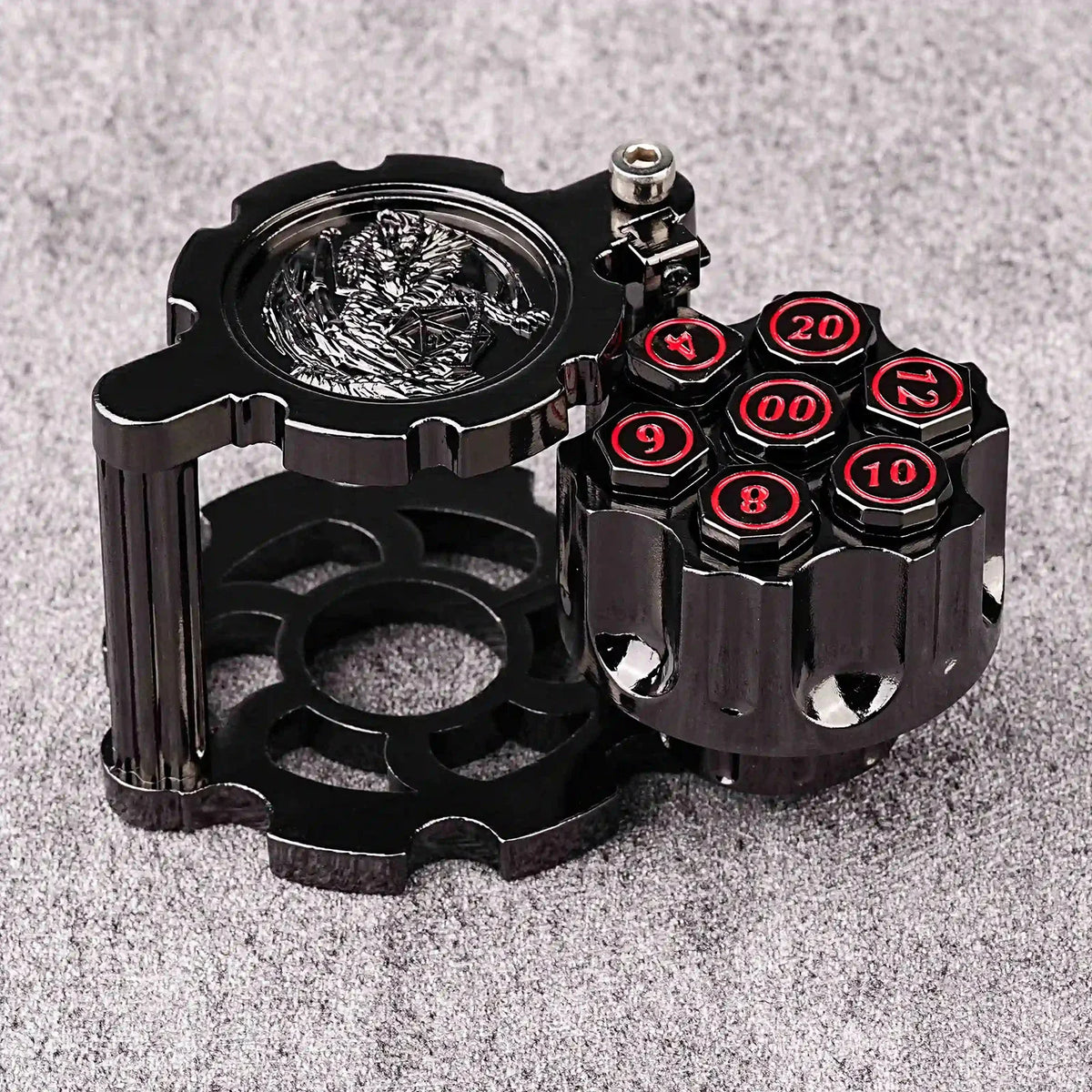 A black revolver-shaped metal dice set with numbered dice and a spinner on a gray surface.