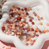 A close-up view of a white dish filled with various colored glass spacer beads including jade, pink, and amber tones.