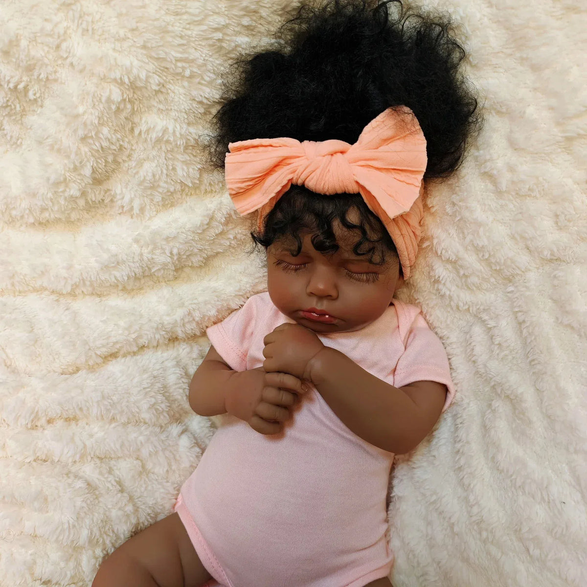 A lifelike 19-inch reborn baby doll with hand-rooted hair wearing a pink onesie and an orange bow