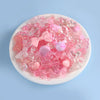 A mix of pink and clear acrylic beads, including bows and hearts, displayed in a white dish for DIY jewelry making.