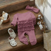 A pink knit ruffle romper for a baby girl with a matching pink bow and accessories displayed on a wooden surface.