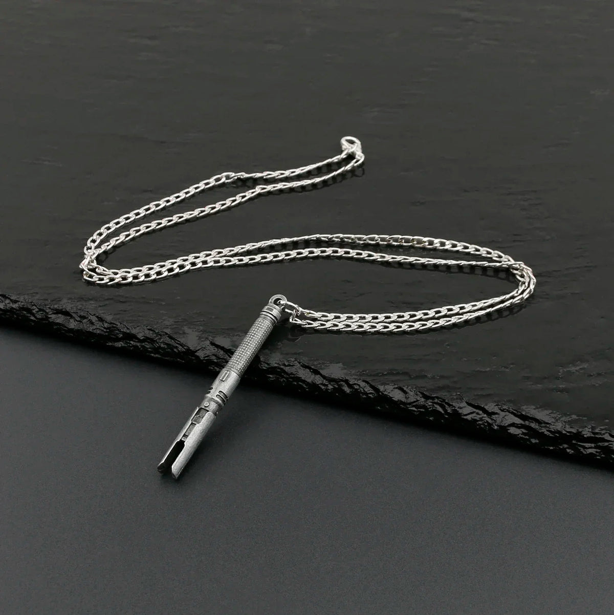 A silver metal saber keychain necklace is displayed on a dark surface.