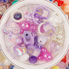A collection of iridescent and pastel acrylic bow and flower beads for DIY jewelry making displayed in a white bowl.