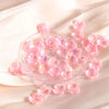 Pink acrylic beads shaped like four-petaled flowers scattered on a white fabric