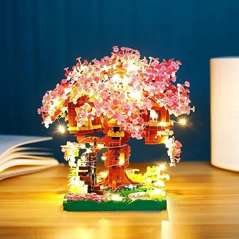 A miniature sakura tree structure built from building blocks illuminated with warm lights on a wooden surface.