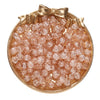 A round gold-toned dish filled with small, pink glass crackle beads for jewelry making.