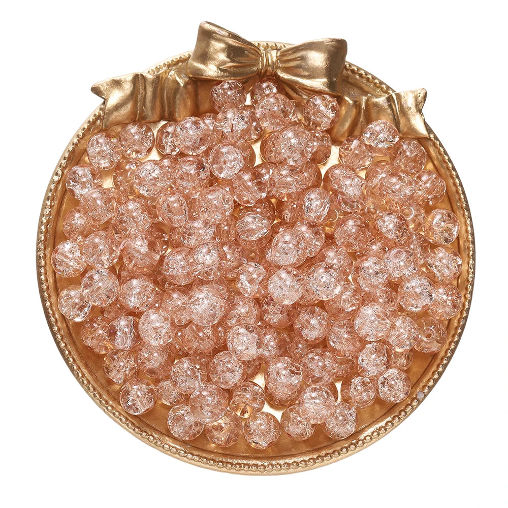 A round gold-toned dish filled with small, pink glass crackle beads for jewelry making.
