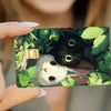 A hand holds a card sticker featuring a cute gray kitten sleeping next to a black cat amidst green leaves.