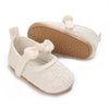 A pair of white lace-trimmed baby girl moccasin shoes with a bow and a tan sole.