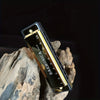 A black harmonica in a gold carrying case rests on a piece of weathered wood.