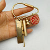 A brass keychain featuring a locking carabiner clip and a circular red and gold charm, held in a hand.